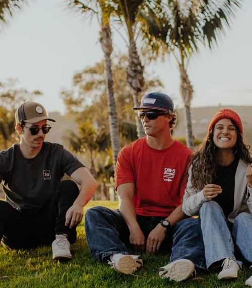 Three people sitting on a grassy hill smiling for the camera