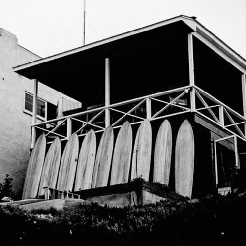 nine surfboards leaning against the porch of a beach house back in the 1950's