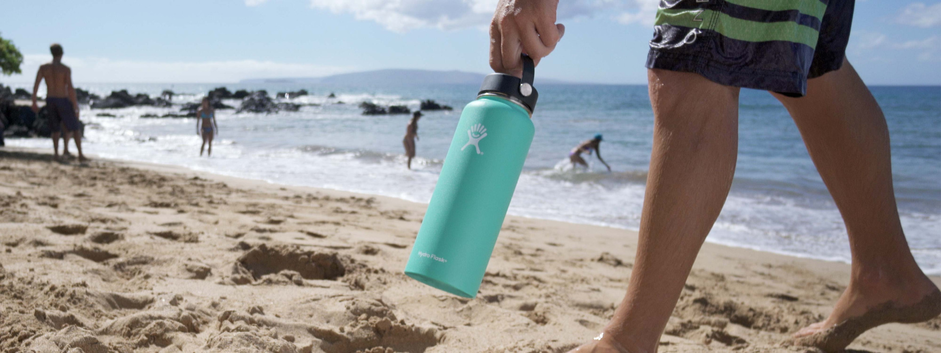 man carrying hydroflask on the beach