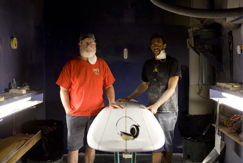 gary larson and the late terry martin standing in front of a surboard in a shaping bay